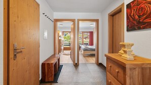 A hallway with wooden doors, a bench, a bed, and a painting of a rose. - Les Platanes E4 - 5 pers - centre station (Haute-Nendaz)