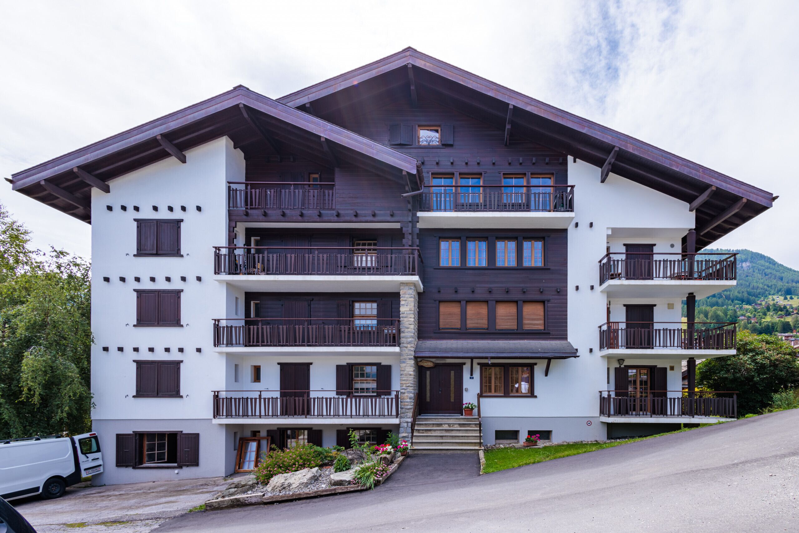 A multi-story building with balconies, a front entrance, and a driveway.