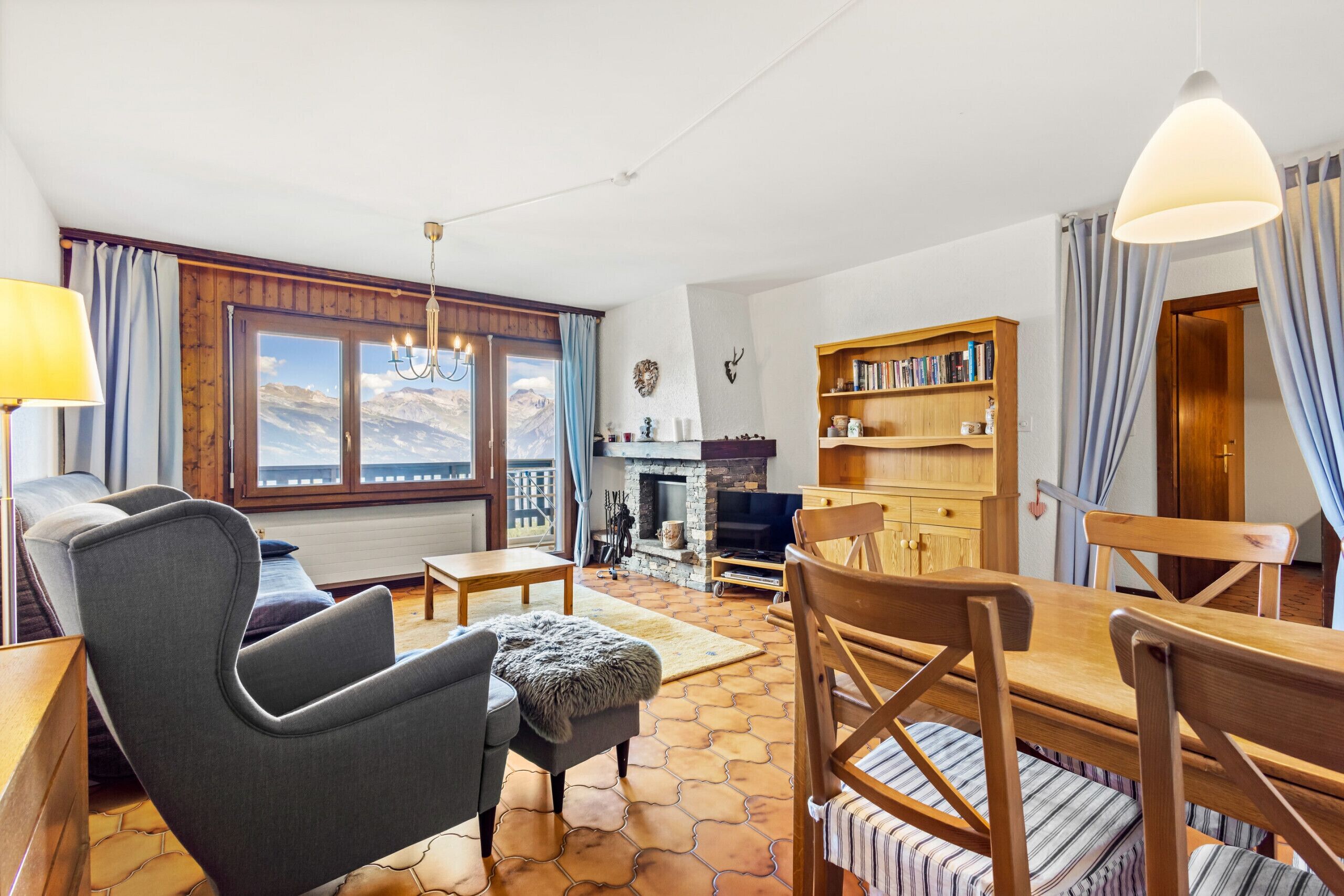 Un salon chaleureux avec une cheminée, une bibliothèque en bois et une vue sur les montagnes, visible à travers de grandes fenêtres.