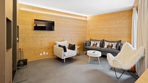 Un salon moderne avec des murs recouverts de panneaux de bois, un canapé blanc, un canapé gris, un fauteuil blanc et une petite table blanche.