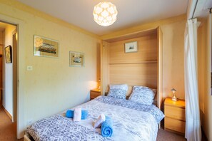 A bedroom with a bed, two bedside tables, a hanging light fixture, and two wall-mounted pictures.