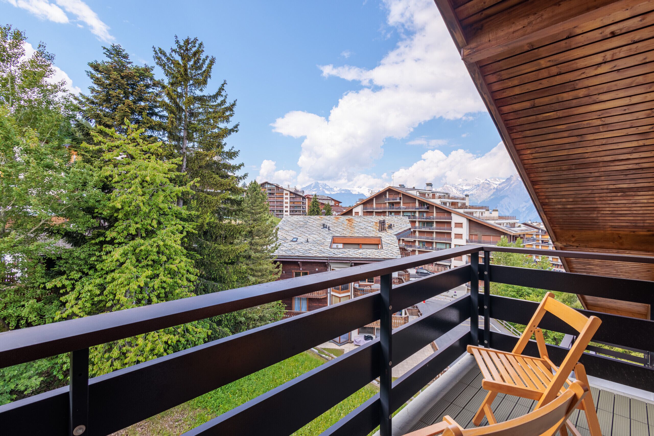 A balcony with a wooden chair, overlooking a mountainous landscape with buildings.