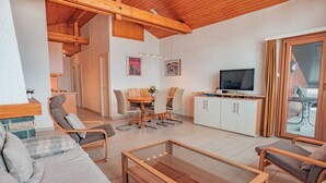 A modern living room with a wooden ceiling, a TV, a dining table with chairs, and a sofa.