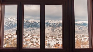 A view through a window with a wooden frame, revealing a snowy mountain landscape and a town below.