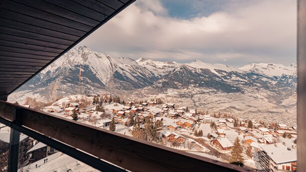 A snow-covered mountain village with wooden buildings and a view of the mountains.