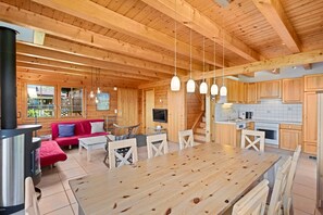 A wooden cabin interior with a dining area, kitchen, and a cozy seating area.