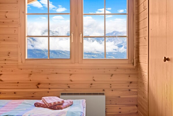 A wooden cabin room with a large window overlooking a mountain range.