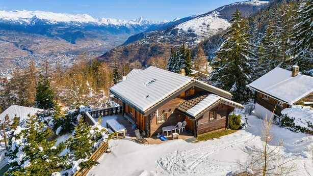 A wooden chalet with a sloped roof, a patio with outdoor seating, and a view of snow-covered mountains. - Gisèle - 8 pers - près des pistes (Haute-Nendaz)