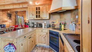 A wooden cabin-style kitchen with a central island, built-in oven, and a large window. - Gisèle - 8 pers - près des pistes (Haute-Nendaz)