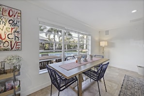 A dining area with a large window, a table with chairs, a decorative wall piece, and a lamp.