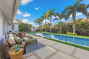 A poolside area with a sofa, chairs, and a table, surrounded by palm trees and a clear sky. - Pet-Friendly Inland Home | Resort Style Yard & Pool (Marco Island)