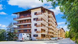 Un hotel de varios pisos con balcones, un estacionamiento y una camioneta estacionada al frente.