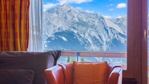 Una habitación con vistas a montañas nevadas a través de una ventana, un sillón de cuero marrón y un cojín rojo.