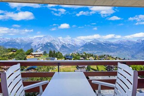 Un balcone con vista su montagne innevate, un tavolo e due sedie.