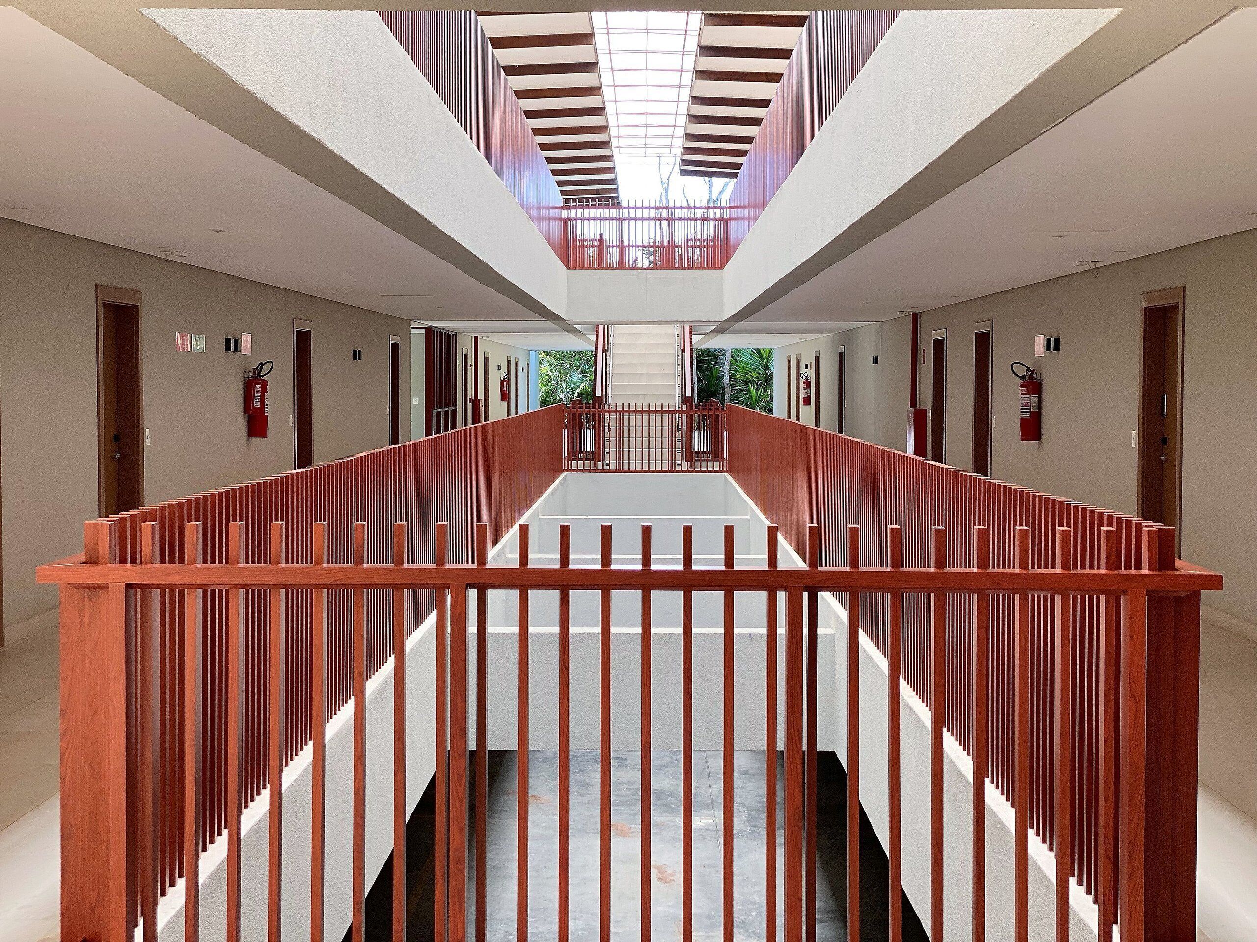A modern hotel corridor with a central staircase, wooden railings, and a skylight.