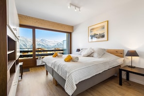 Une chambre avec une grande fenêtre, un lit, un bureau et une vue sur les montagnes.
