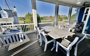 A covered outdoor deck with a wooden table and white chairs, overlooking a residential area. - Bayside Resort * 4BR Luxury Resort Home (Selbyville)