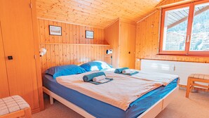 A wooden-paneled room with a bed, a chair, and a window with a view of buildings. - Muverans II F5 - 8 pers - duplex (Haute-Nendaz)
