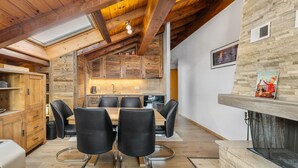 A modern kitchen with wooden cabinets, a dining area with black chairs, and a fireplace. - Les Hauts-de-Nendaz A C5 - 5 pers - ski In&Out (Haute-Nendaz)