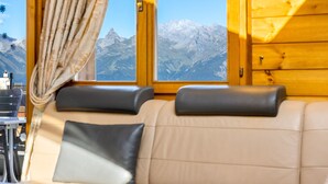 A cozy cabin interior with a leather sofa, a window with a mountain view, and wooden walls. - Les Hauts-de-Nendaz A C5 - 5 pers - ski In&Out (Haute-Nendaz)