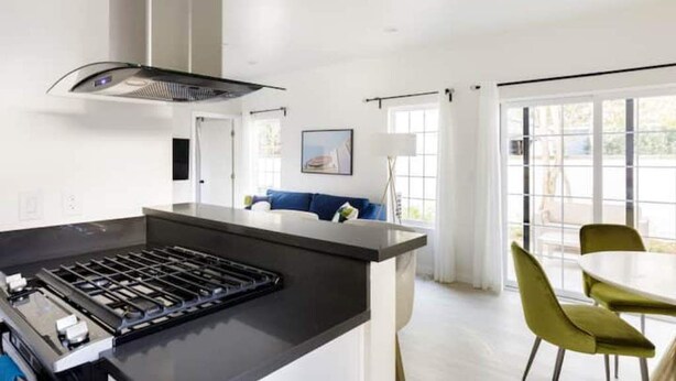 A modern kitchen with a central island, a dining area with a round table and chairs, and a large window providing natural light. - NoHo Toluca Lake Luxury Near Universal Studios  (Los Angeles)