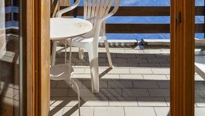 A wooden balcony with a white plastic chair and table, overlooking a snowy mountain landscape.