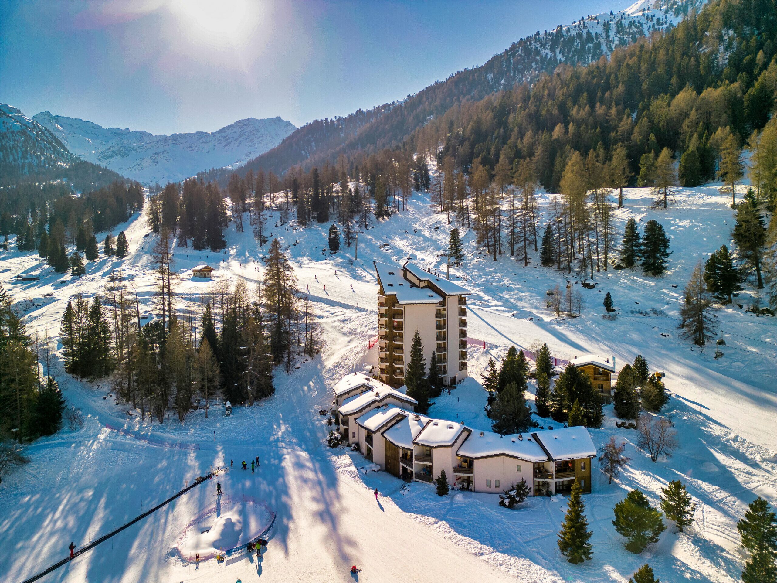 A snow-covered mountain resort with a ski lift, a building with multiple floors, and surrounding trees.