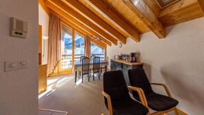 A wooden interior with a dining area, chairs, a table, and a view of mountains through a window.
