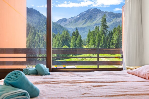 A bedroom with a bed, a window with a mountain view, and a pair of towels on the bed.