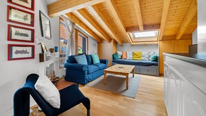 Ein modernes Wohnzimmer mit hoher Decke, Holzbalken, einer Couch, einem Couchtisch und einer Küchenzeile.