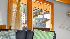 Ein Zimmer mit einer Couch, einem Fenster mit Vorhängen und Blick auf Gebäude.