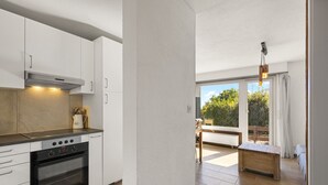 Une cuisine moderne avec des meubles blancs, un four encastré et un coin repas comprenant une table et un banc en bois.