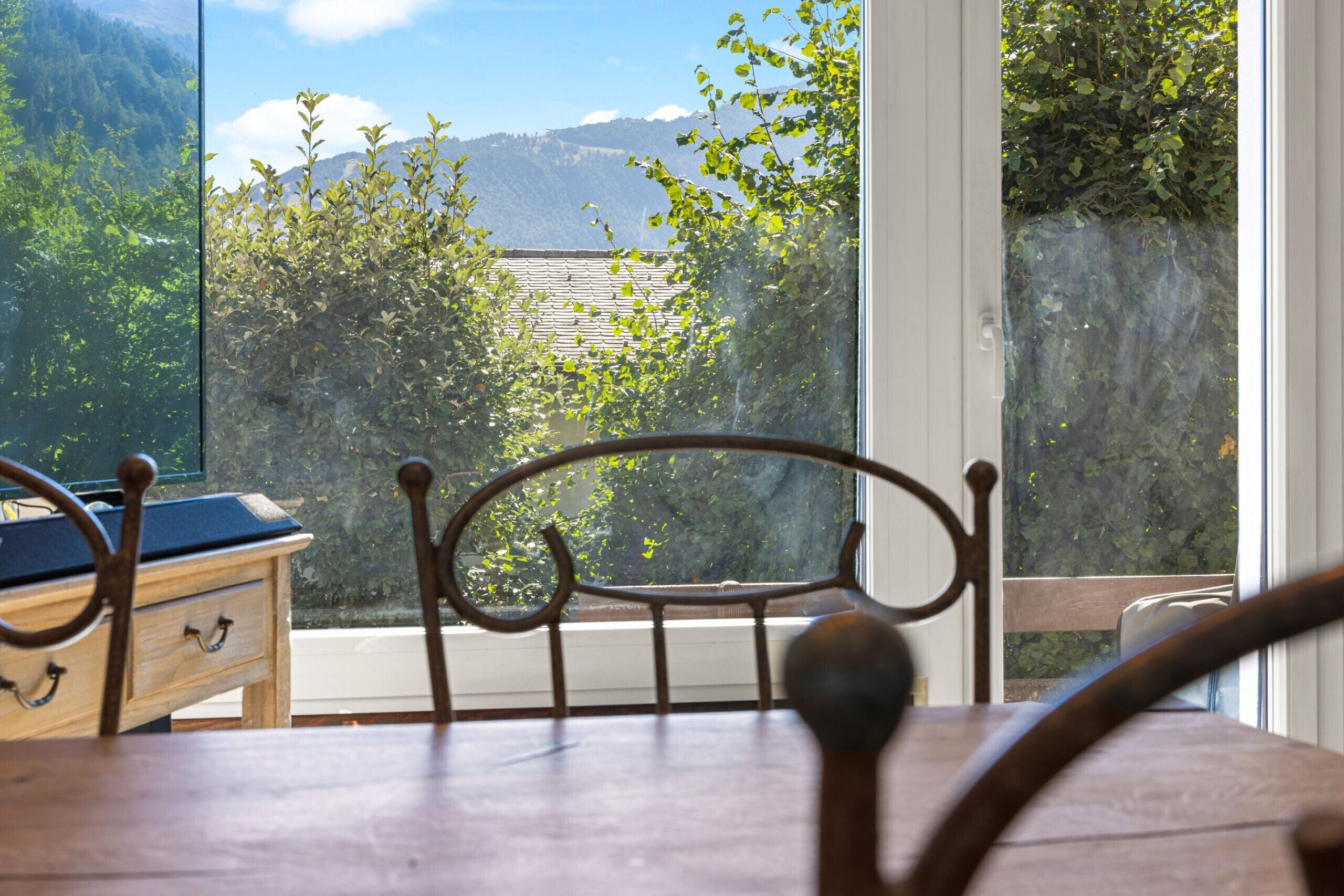 A wooden dining table with a metal chair in front of a window overlooking a mountainous landscape.