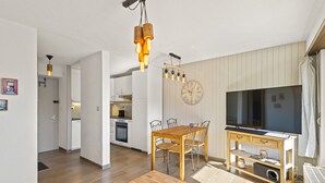 Une cuisine moderne avec des meubles en bois, un coin repas avec une table et des chaises en bois, un téléviseur et une horloge au mur.
