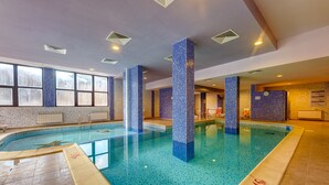 Una piscina interior con suelo y paredes de azulejos, ventanas amplias e iluminación empotrada en el techo.