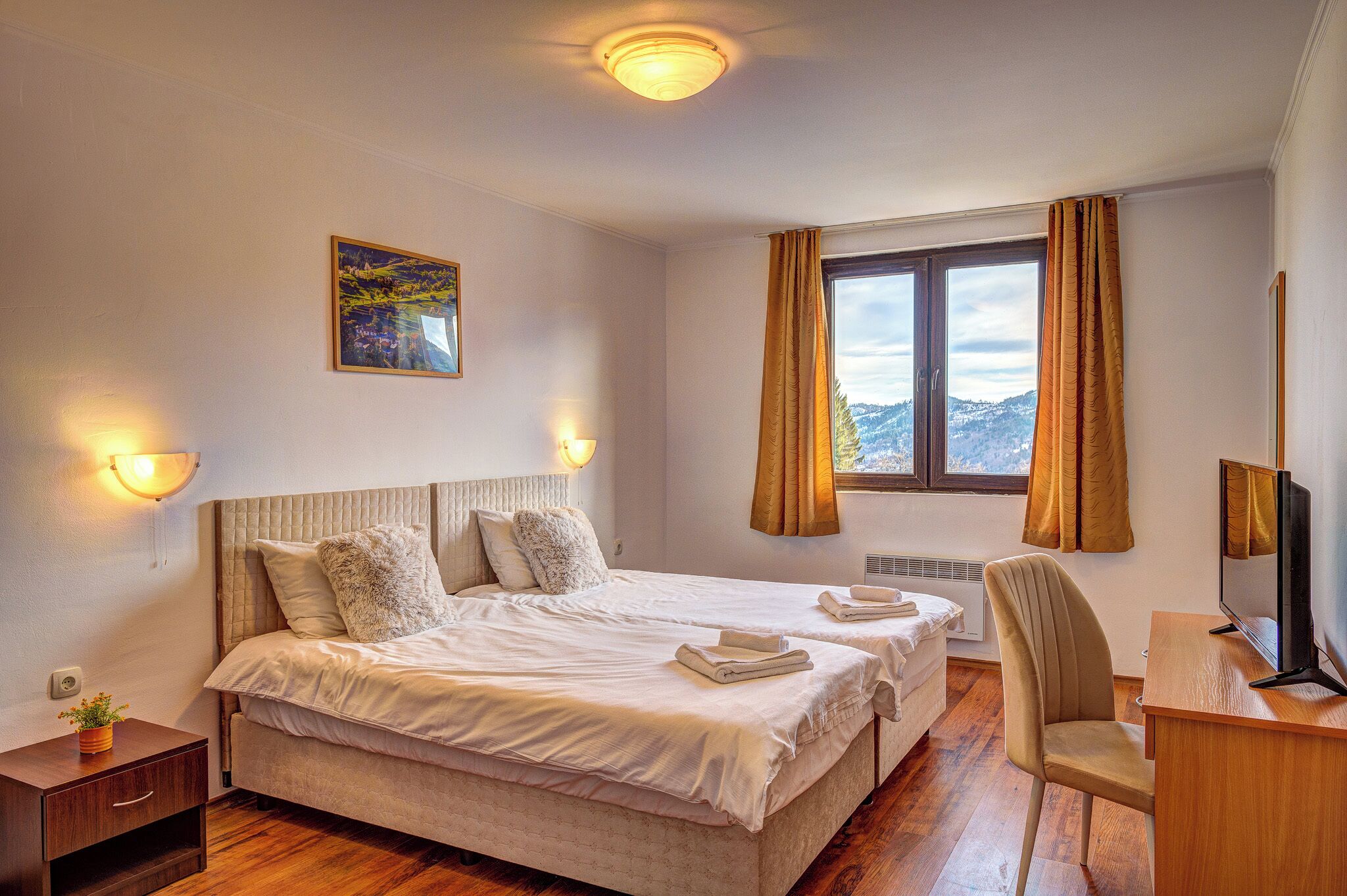 Habitación de hotel con dos camas, un escritorio con computadora, un televisor, una ventana con cortinas y un cuadro en la pared.