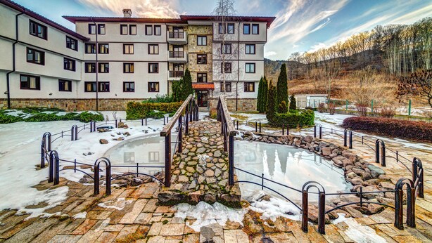 Un hotel de varios pisos con fachada de piedra, un patio central con piscina y montañas al fondo.