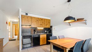 A modern kitchen with wooden cabinets, a built-in oven, and a dining area with a wooden table and chairs. - Les Hauts-de-Nendaz B L7 - 4 pers - ski In/Out (Haute-Nendaz)