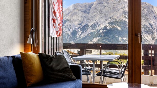 A room with a view of mountains, a wooden floor, a blue sofa, and a table with chairs. - Les Hauts-de-Nendaz B L7 - 4 pers - ski In/Out (Haute-Nendaz)
