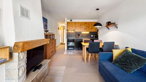 A modern living room with a stone fireplace, a blue sofa, and a dining area with wooden chairs and a table. - Les Hauts-de-Nendaz B L7 - 4 pers - ski In/Out (Haute-Nendaz)
