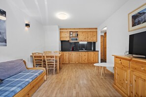Un espacio habitable compacto con kitchenette, sofá, mesa de comedor y televisor.