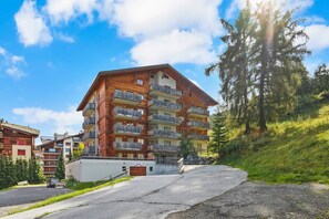 A multi-story hotel with balconies, a parking area, and a hillside backdrop.
