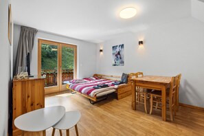 Una habitación con una cama, una mesa, sillas, un armario de madera y una ventana con cortinas.