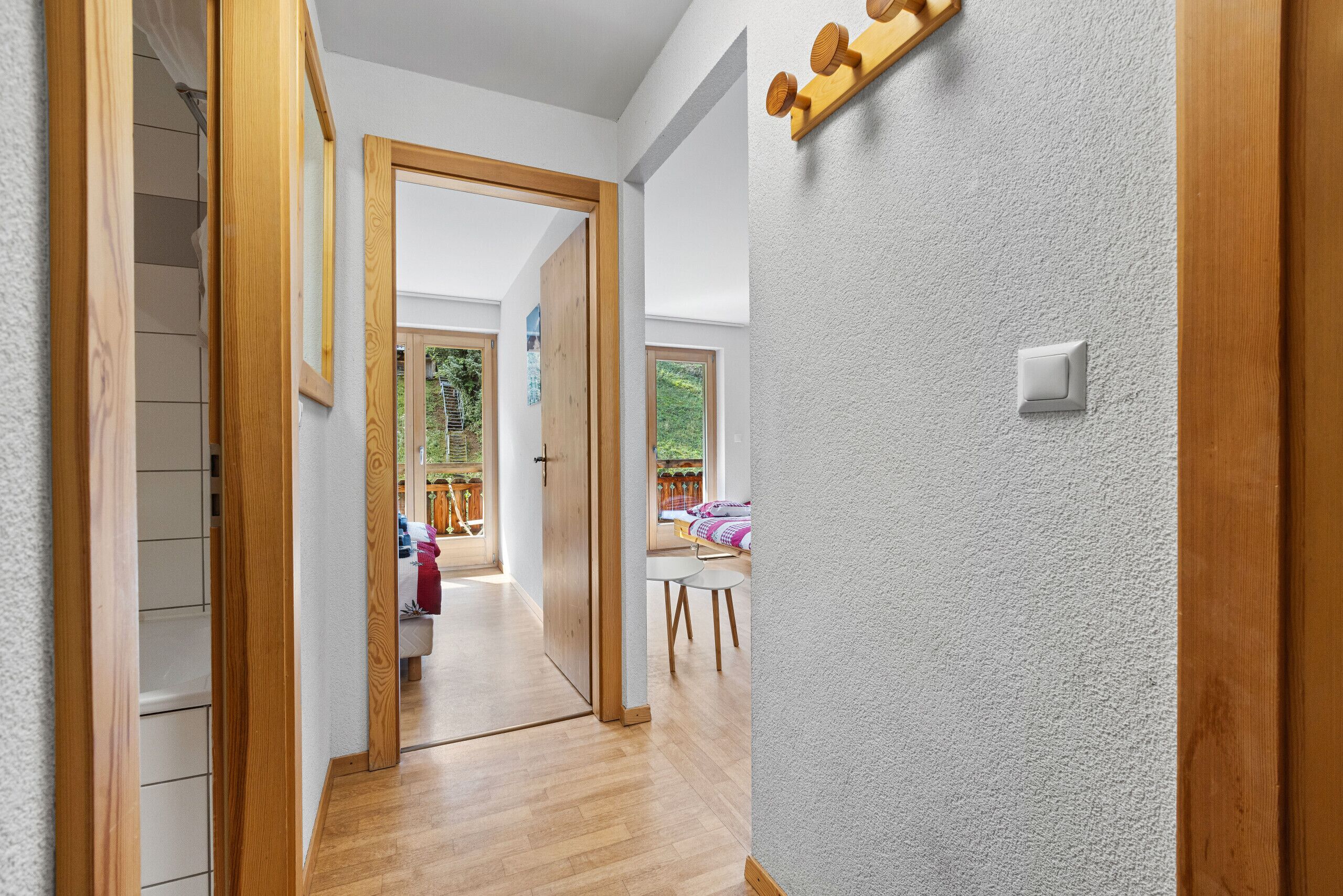 A hallway with wooden flooring, a white textured wall, and a door leading to a room with a view.