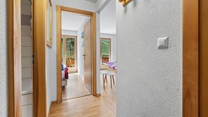 Um corredor com piso de madeira, parede branca texturizada e uma porta que dá para um quarto com vista.