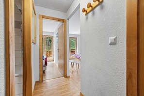 A hallway with wooden flooring, a white textured wall, and a door leading to a room with a view.