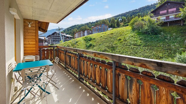 Uma varanda com mesa e cadeiras, com vista para uma colina com edifícios.