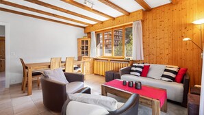 A cozy living area with wooden beams, a sofa, chairs, a dining table, and a view of a mountain through large windows. - Le Torrent 26 - 6 pers - au calme (Haute-Nendaz)