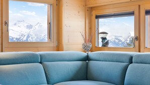 A corner sofa in a wooden cabin with large windows offering a mountain view.