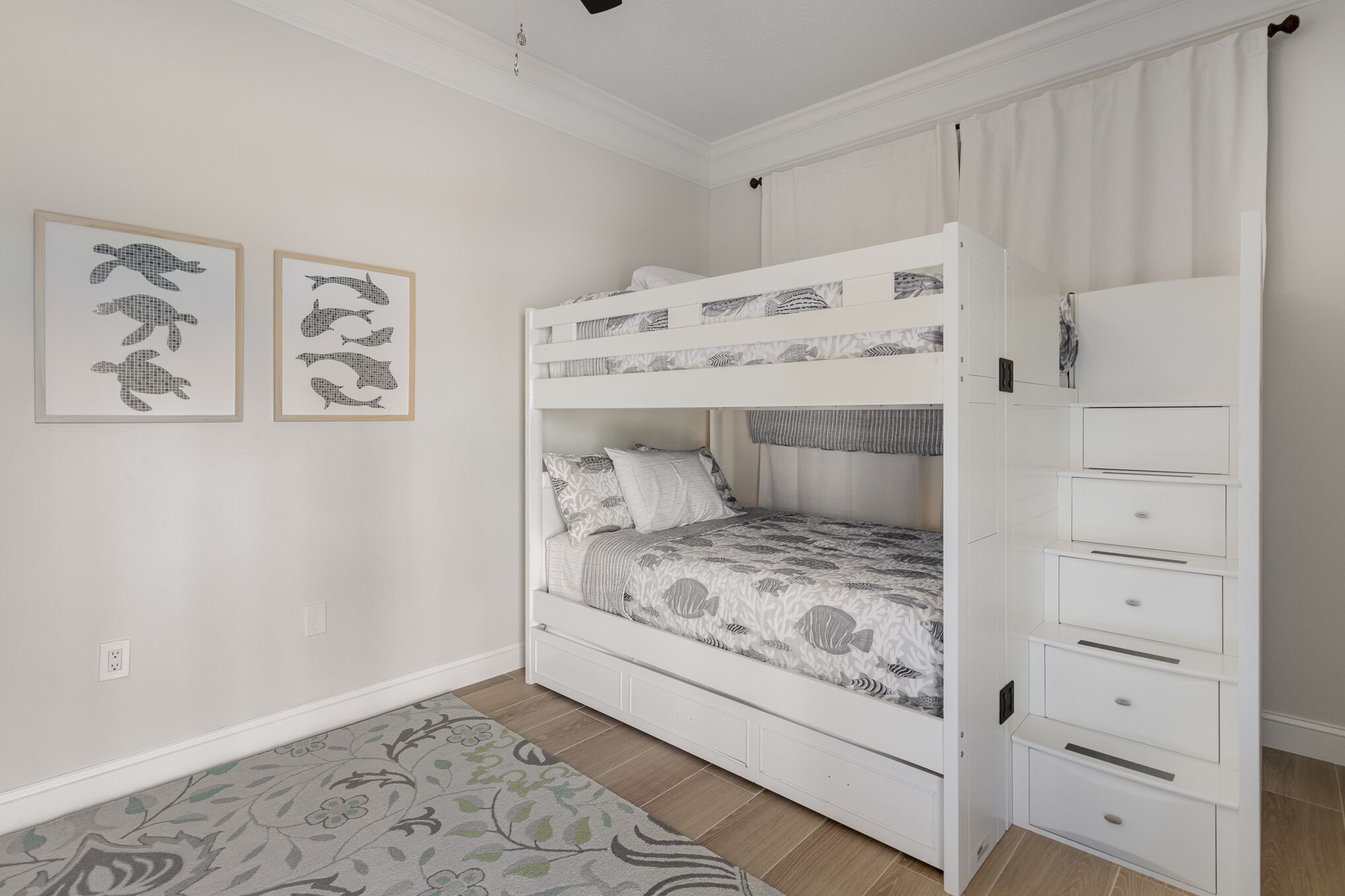 Ein Stockbett mit einer Ablage daneben, ein gemustertes Teppich und zwei gerahmte Bilder an der Wand.